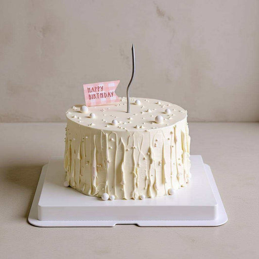 Minimalist ivory birthday cake with textured buttercream, white pearl decorations, pink Happy Birthday flag, and silver candle