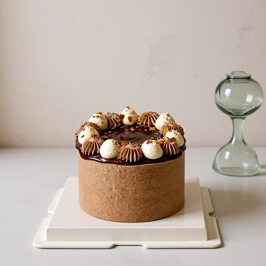 Mocha Harmony Cake topped with glossy chocolate glaze and decorative cream, presented on a modern cake stand.
