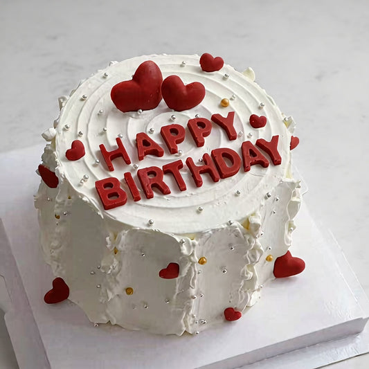 Sweetheart celebration cake decorated with red hearts and 'Happy Birthday' text on white whipped cream.