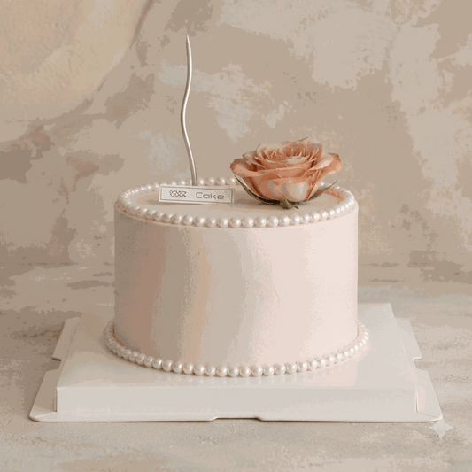 Elegant blush pink Pearl & Rose Cake with edible pearl borders, fresh dusty rose, and silver candle centerpiece