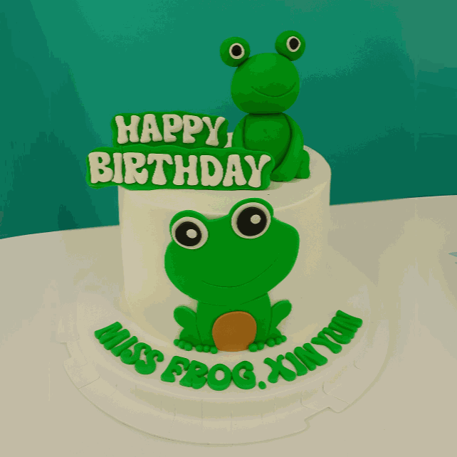 Green frog cake with 3D frog topper, happy birthday plaque, and custom lettering on white cream frosting