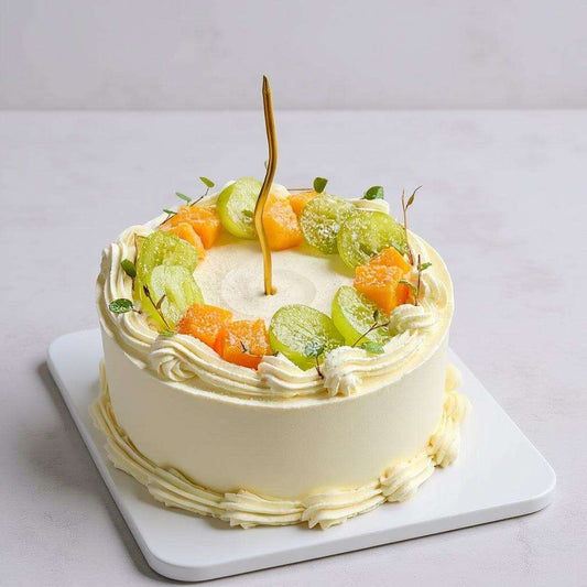 Golden cake topped with Shine Muscat grapes, mango cubes, and a twisted gold candle