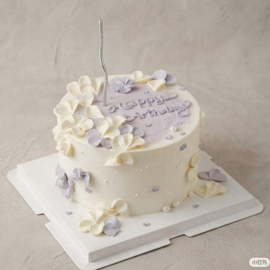Lilac & ivory cake Singapore with hand-piped pastel petals, sugar pearls, cursive "Happy Birthday" topping, and silver candle