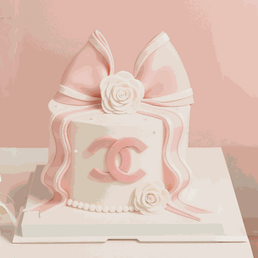 Luxury pastel pink Bow Cake with oversized 3D fondant bow, white camellia roses, and pink interlocking CC emblem on ivory cream frosting