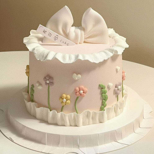Pastel pink bow cake with ruffled white cream and pastel wildflower decorations